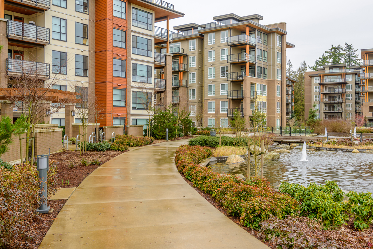 entrance to apartment community with walkways along a lake and fountain